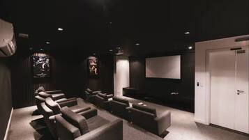 Een filmzaal in donkere kleuren met meerdere rijen stoelen, een groot scherm en een deur.