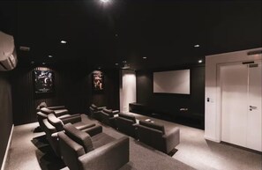 A dark-themed cinema room with multiple rows of seats, a large screen, and a door. - Flipchave - Apartamentos Highline design (Joinville)