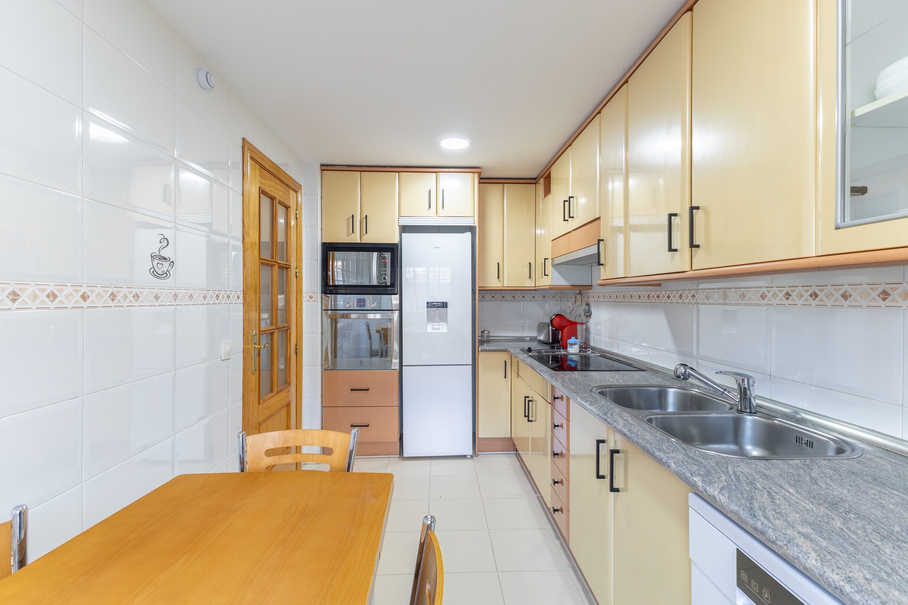 Una cocina con microondas, refrigerador, lavabo y mesa de madera.