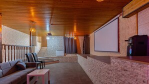 A cozy indoor seating area with a sofa, chairs, a table, a projector screen, and a brick wall. - Semi-detached chalet for up to 12 guests, Pool, BBQ (Loeches)