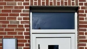 A white door with a glass panel, a keypad, and a small mailbox on a brick wall. - Modern comfort in the heart of Bocholt - Stylish apartment for up to 4 guests (Bocholt)