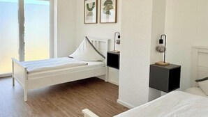 A bedroom with a bed, a bedside table, a nightstand, a wall-mounted lamp, and two framed pictures. - Modern comfort in the heart of Bocholt - Stylish apartment for up to 4 guests (Bocholt)