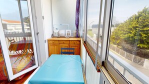 En balkong med ett bord och stolar, ett litet träskåp och en säng med ett blått överdrag.