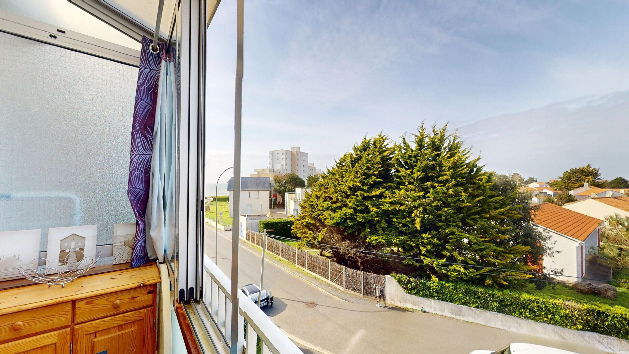 A window with a view of a residential area, a large tree, and a street.