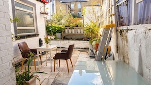 Un espace patio avec une table en verre, deux chaises marron et des plantes en pot.