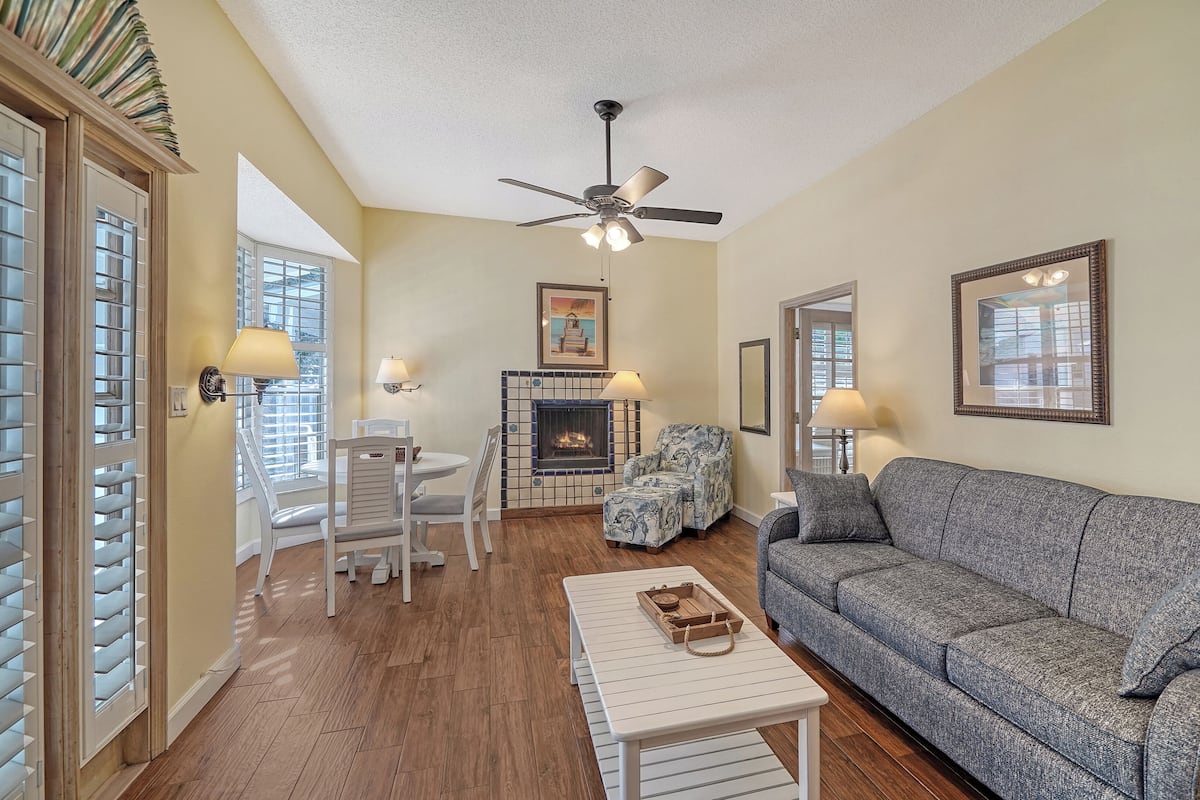 A living room with a fireplace, a sofa, a coffee table, and a dining area with chairs and a table.
