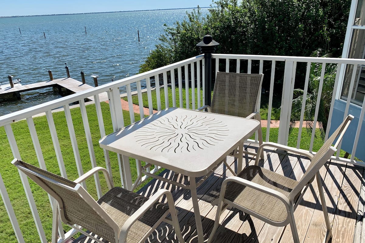 A deck with a table and chairs, overlooking a body of water.