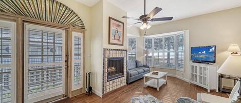 A living room with a fireplace, a television, and a ceiling fan.