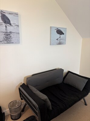 Ein kleines Zimmer mit einem Bett, einem Mülleimer und zwei an der Wand hängenden Vogelbildern.