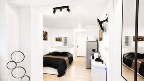 Un dormitorio moderno con cama, escritorio, espejo y refrigerador.