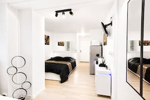 Quarto moderno com cama, escrivaninha, espelho e frigorífico.