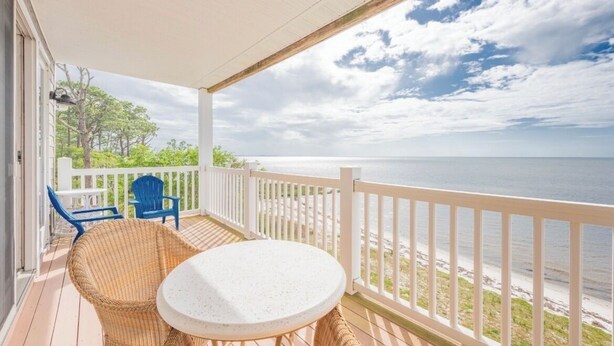 A covered balcony with a white railing, wicker furniture, and a view of the ocean. - Enjoyable 2-bedroom waterfront condo in charming Carrabelle (Carrabelle)