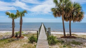 A wooden boardwalk leading to the beach with palm trees on either side. - Enjoyable 2-bedroom waterfront condo in charming Carrabelle (Carrabelle)