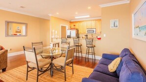 A living room with a blue sofa, a dining table with chairs, a kitchen area with wooden cabinets, and a microwave. - Enjoyable 2-bedroom waterfront condo in charming Carrabelle (Carrabelle)