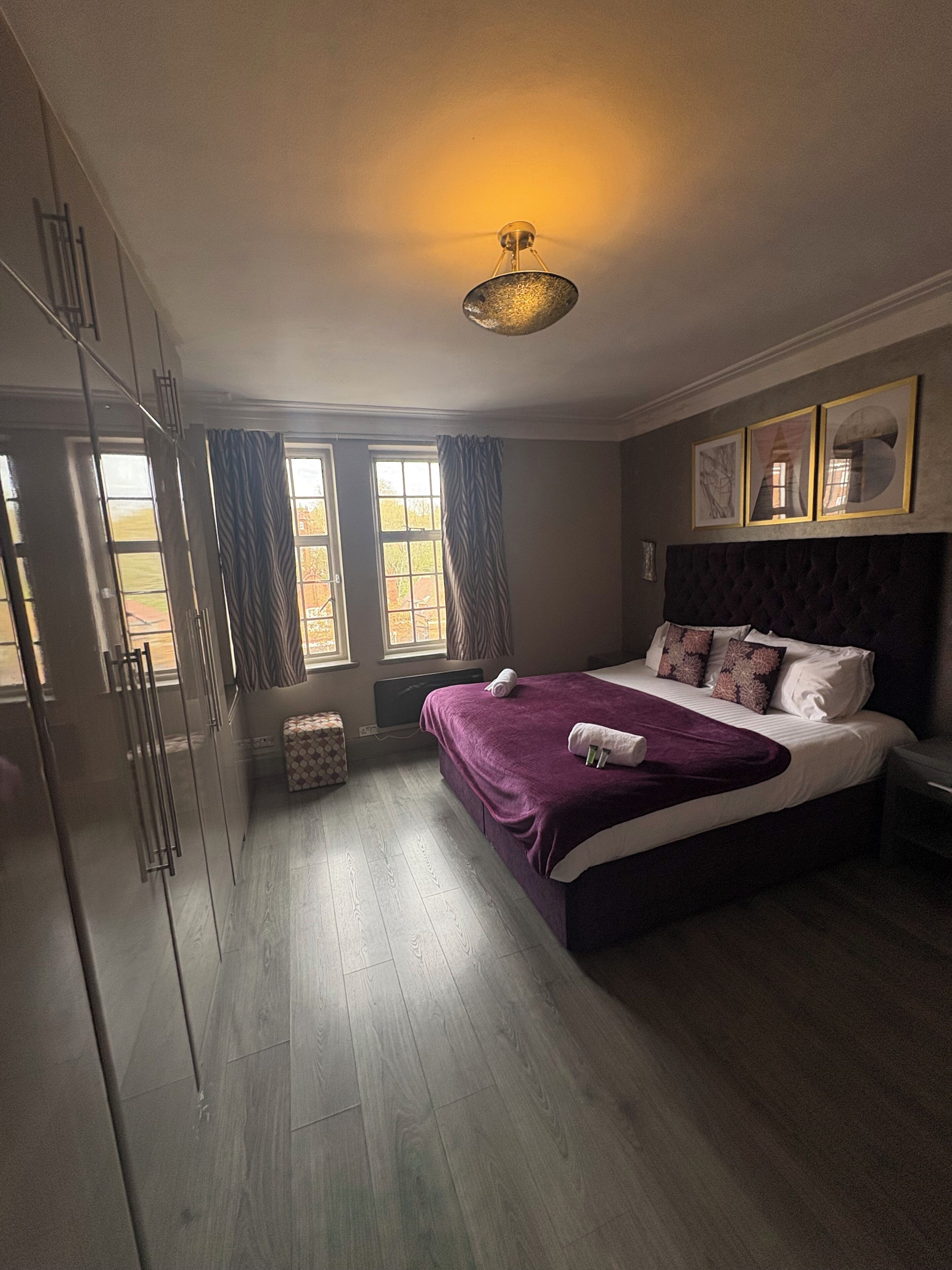A bedroom with a bed, a wardrobe, a window with curtains, and a wall-mounted light fixture.