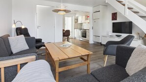 A modern living room with a sofa, armchairs, a wooden coffee table, and a dining table. There is a kitchen in the background with white cabinets and a TV mounted above the counter. - "Amlethus" - 2.3km from the sea by Interhome (Rømø)