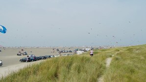 A beach with a path leading through tall grass, cars parked along the shore, and a clear sky with kites flying. - "Amlethus" - 2.3km from the sea by Interhome (Rømø)