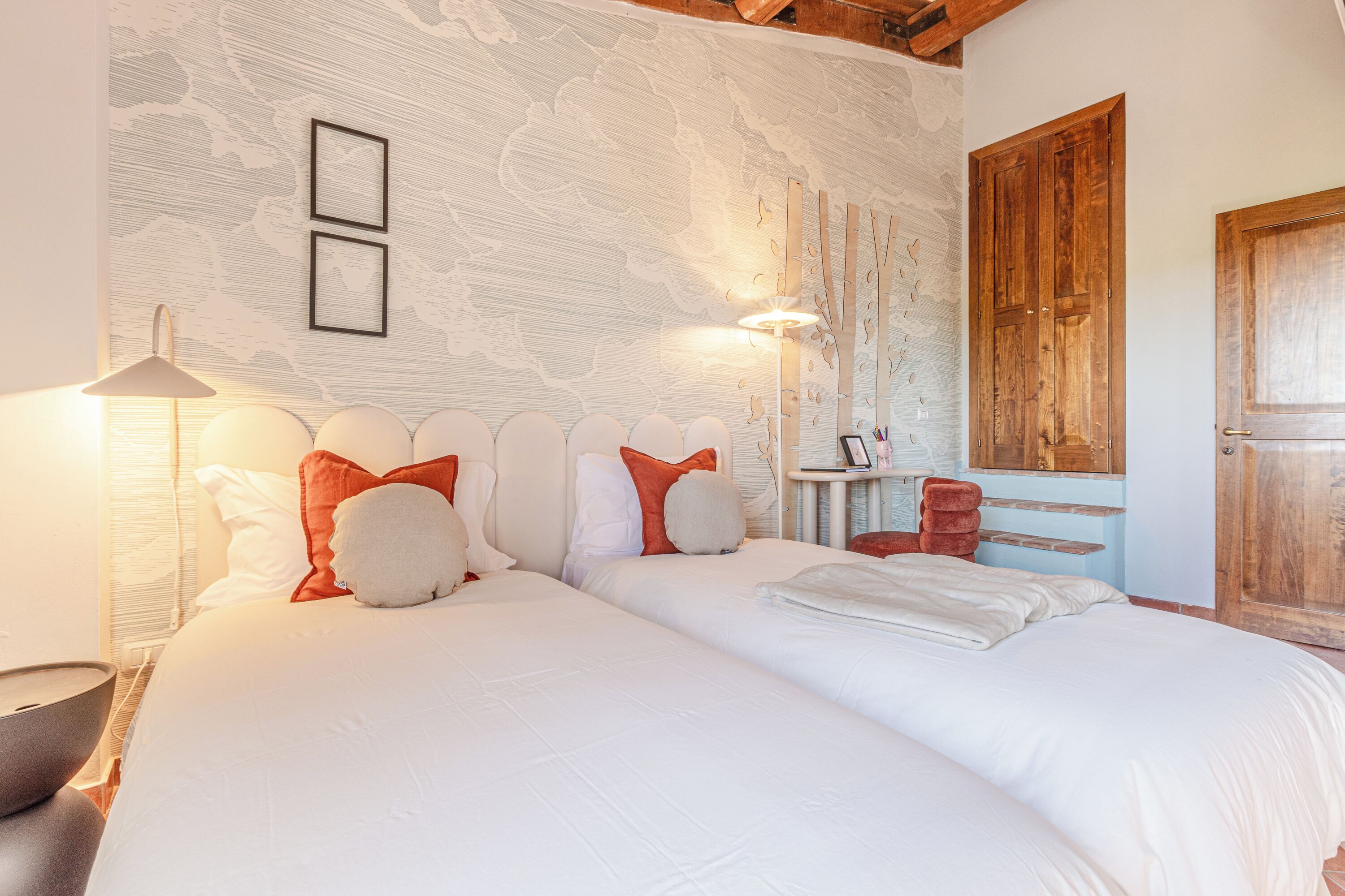 Een slaapkamer met twee bedden, een houten garderobe, een nachtkastje en een wandlamp.