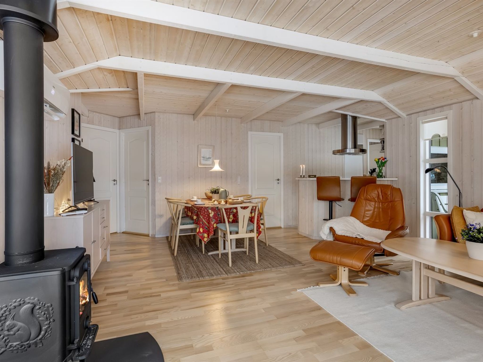 Un salon chaleureux avec une cheminée, un plancher en bois, un coin repas avec une table et des chaises, et un espace détente avec un canapé et un fauteuil.
