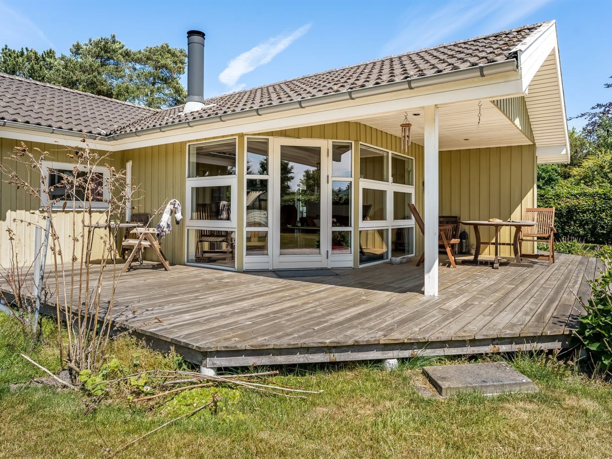 Ein Haus mit einer Holzdachterrasse, großen Glasfenstern und einem Schornstein.