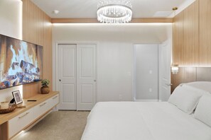 Ein Schlafzimmer mit einem Bett, einem an der Wand montierten Fernseher, einer Chandelüster und Holzvertäfelung.