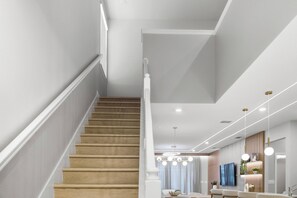Eine Treppe führt zu einem modernen Wohnbereich mit einem Esstisch, Stühlen, einem Fernseher und Pendelleuchten.