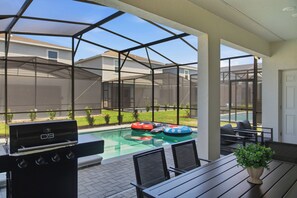 En täckt uteplats med grill, pool och en avslappningshörna.