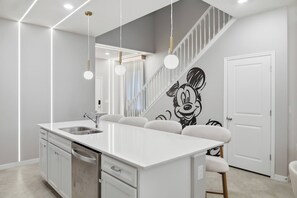 Eine moderne Küche mit einer zentralen Kochinsel, Edelstahlgeräten und einem Wandbild mit Mickey Mouse.