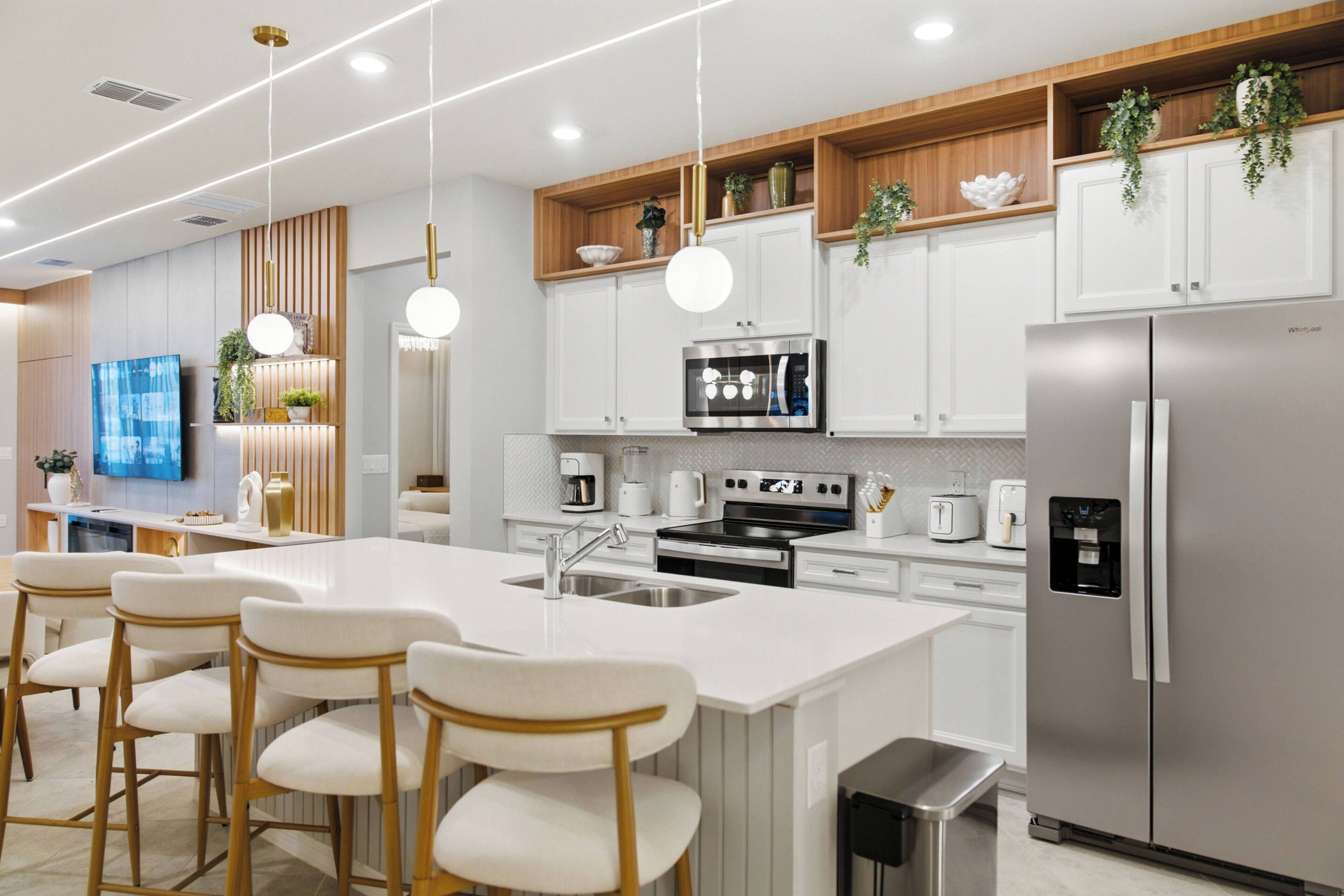 A modern kitchen with white cabinetry, stainless steel appliances, and a central island with bar stools.