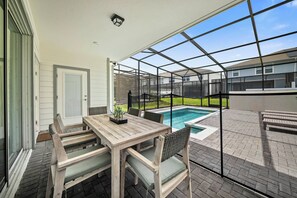 A covered patio with a wooden table and chairs, a pool, and a view of neighboring houses. - 5BR house sleeps 12 with game room and pool (Davenport)