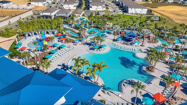 Ett flygbildsfoto av ett semesterområde med en central pool, flera vattenrutschbanor och solstolar.