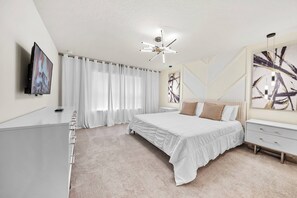A modern bedroom with a bed, bedside tables, a TV, and artwork on the walls. - 5BR house sleeps 12 with game room and pool (Davenport)