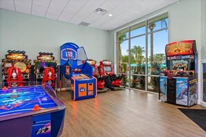 Ein Raum mit Spielautomaten, einem Billardtisch und großen Fenstern mit Blick auf Palmen.