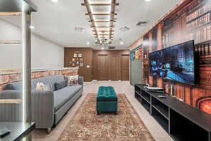 Step into a cozy living area where a plush gray sofa complements a striking bookshelf mural, creating a warm atmosphere. The inviting teal ottoman adds a pop of color, while modern lighting enhances the room's welcoming vibe. - 5BR townhouse sleeps 10 with private pool (Davenport)