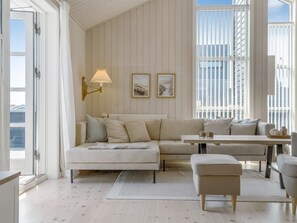 A room with a white sofa, a small table, a lamp, and framed pictures on the wall.