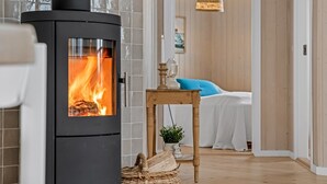A modern interior with a wood-burning stove, a wicker basket, and a bed with a blue pillow.