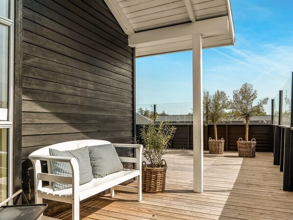 Une terrasse en bois avec un banc blanc, des paniers en osier et une plante en pot.