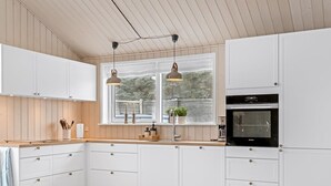 A modern kitchen with white cabinets, a wooden countertop, an oven, and pendant lights.