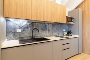 A modern kitchen with a black sink, wooden cabinets, a microwave, and a stone backsplash. - Flower Residence - Appartamento Mimosa (Lissone)