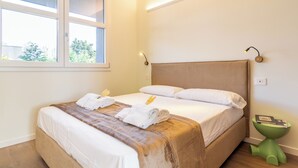A hotel room with a bed, a window, a bedside table, and a green floor lamp. - Flower Residence - Appartamento Hibiscus (Lissone)
