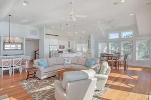 A spacious living area with a large sofa, dining table, and kitchen in the background. - JL #714 - Sunset Splendor -  Luxurious Soundfront Home - Hot tub - Elevator (Kill Devil Hills)