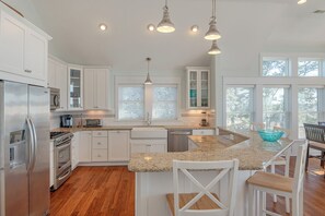 A modern kitchen with white cabinetry, stainless steel appliances, granite countertops, and pendant lighting. - JL #714 - Sunset Splendor -  Luxurious Soundfront Home - Hot tub - Elevator (Kill Devil Hills)