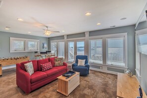 A living room with a red sofa, a blue armchair, a foosball table, and a ceiling fan. - JL #714 - Sunset Splendor -  Luxurious Soundfront Home - Hot tub - Elevator (Kill Devil Hills)