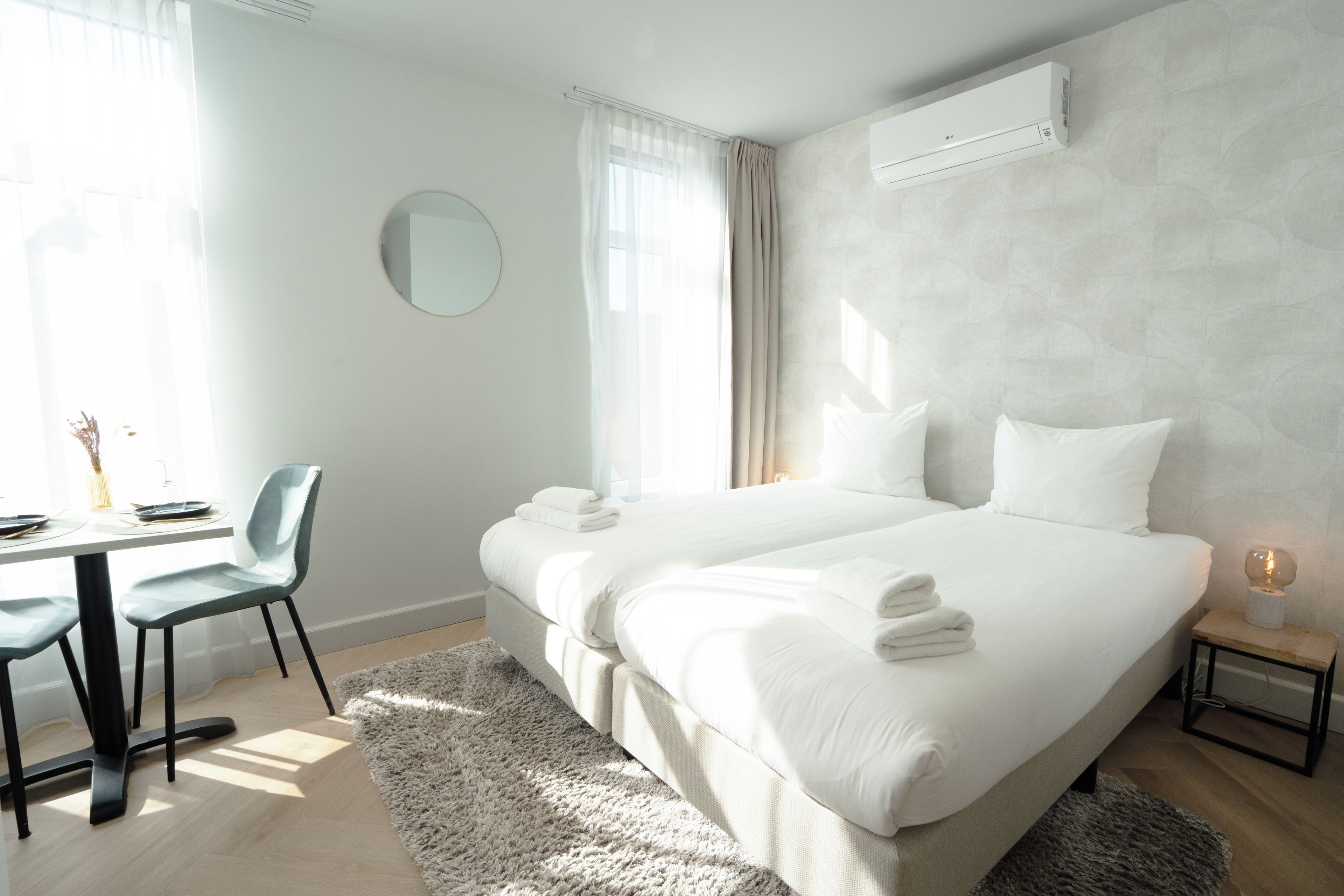 Habitación de hotel con cama, mesita de noche, silla y un espejo redondo en la pared.