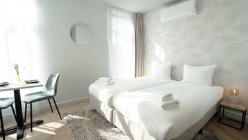 Habitación de hotel con cama, mesita de noche, silla y un espejo redondo en la pared.