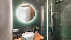 A modern bathroom with a round mirror, a sink, a shower, and a potted plant.