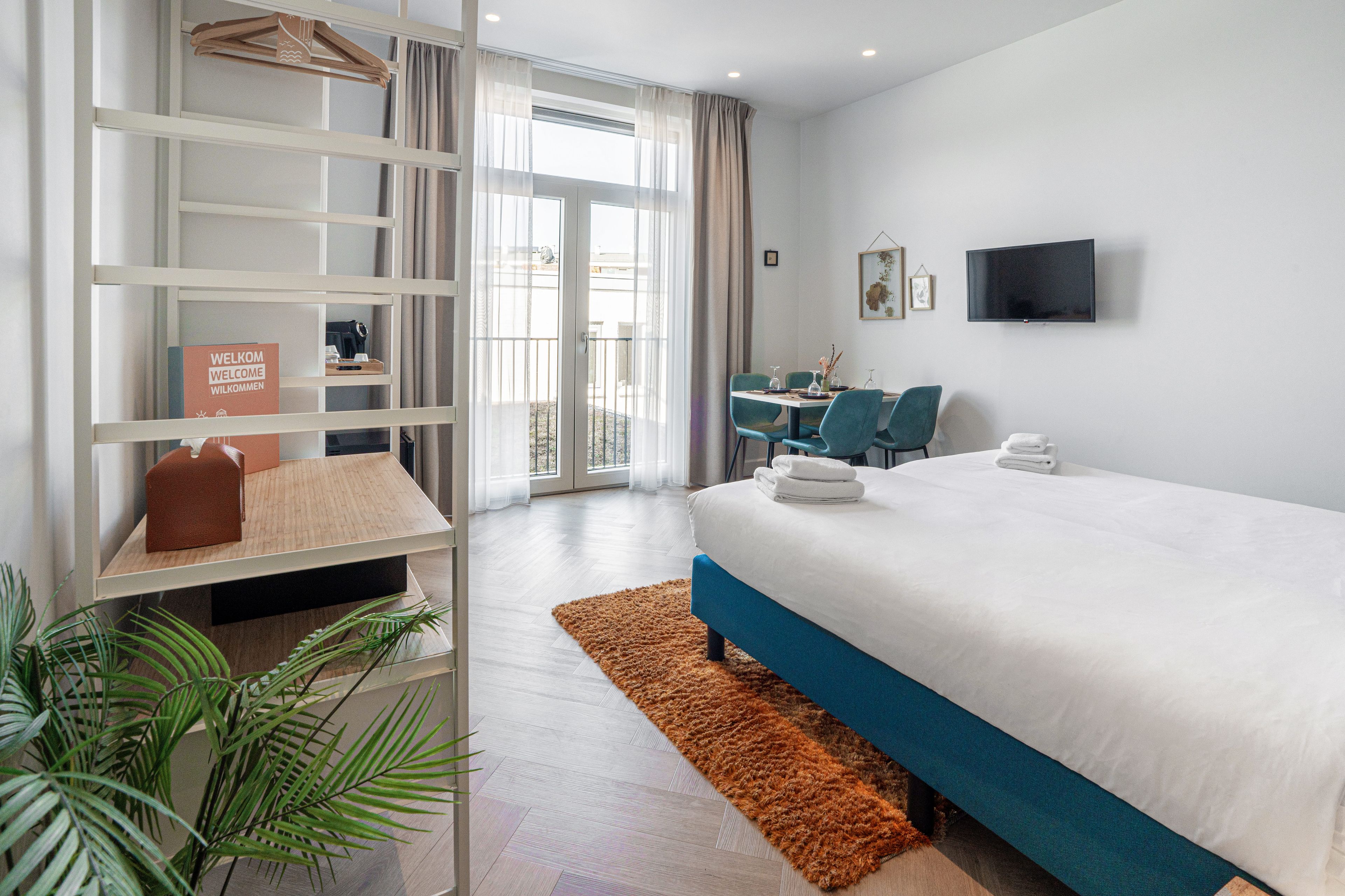 Une chambre d’hôtel équipée d’un lit, d’un bureau, d’une chaise, d’une télévision et d’un balcon avec des rideaux.