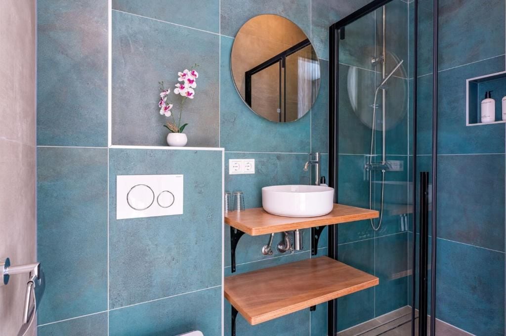 A bathroom with a glass shower enclosure, a white sink, and a wooden shelf.