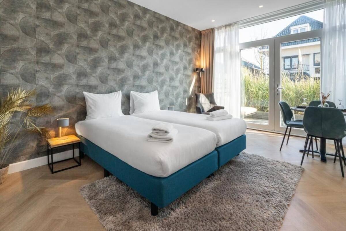 A modern bedroom with a large bed, a nightstand, a lamp, and a view of the outdoors.