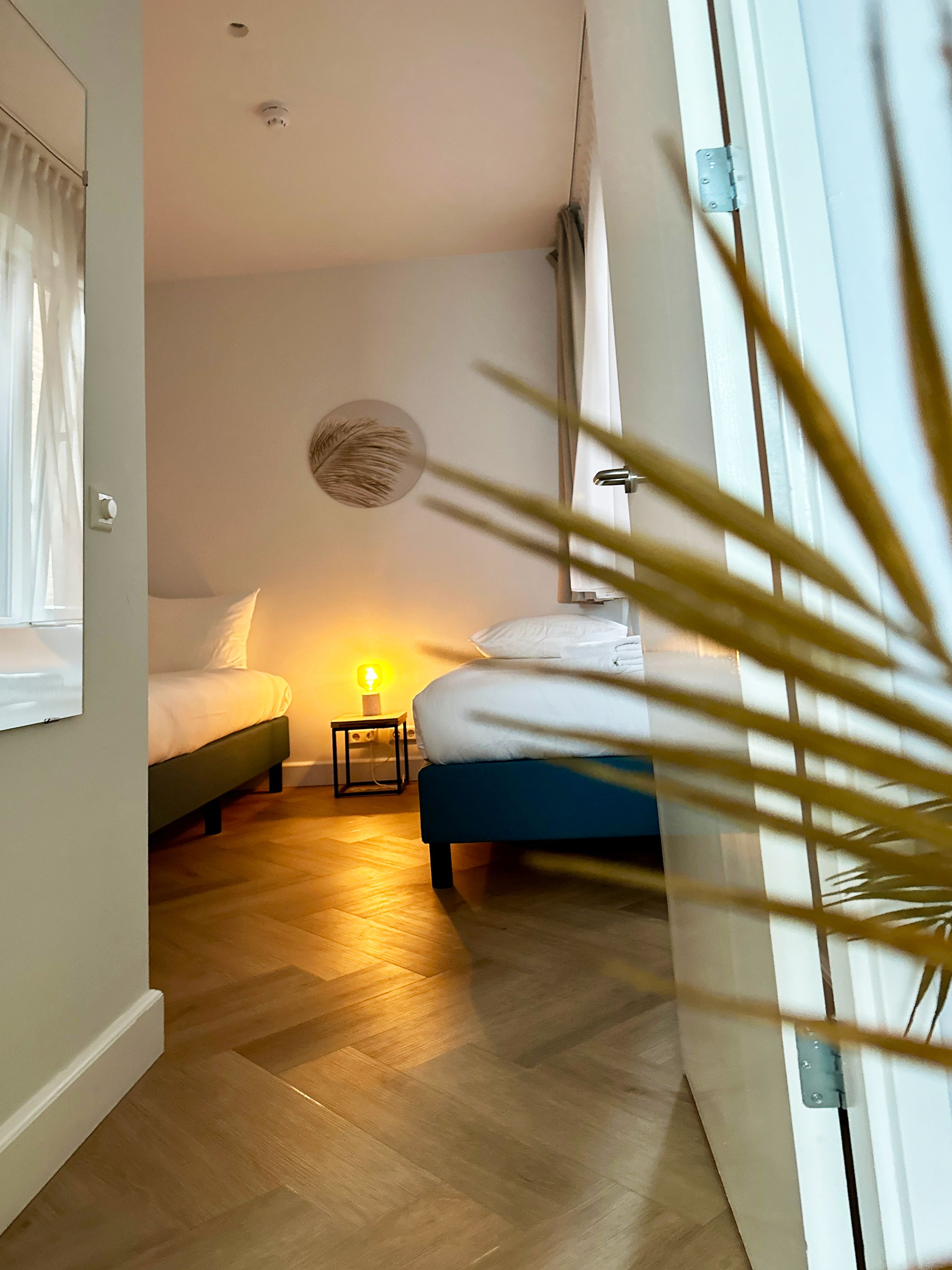Une chambre avec deux lits, une table de chevet avec une lampe et un luminaire fixé au mur.